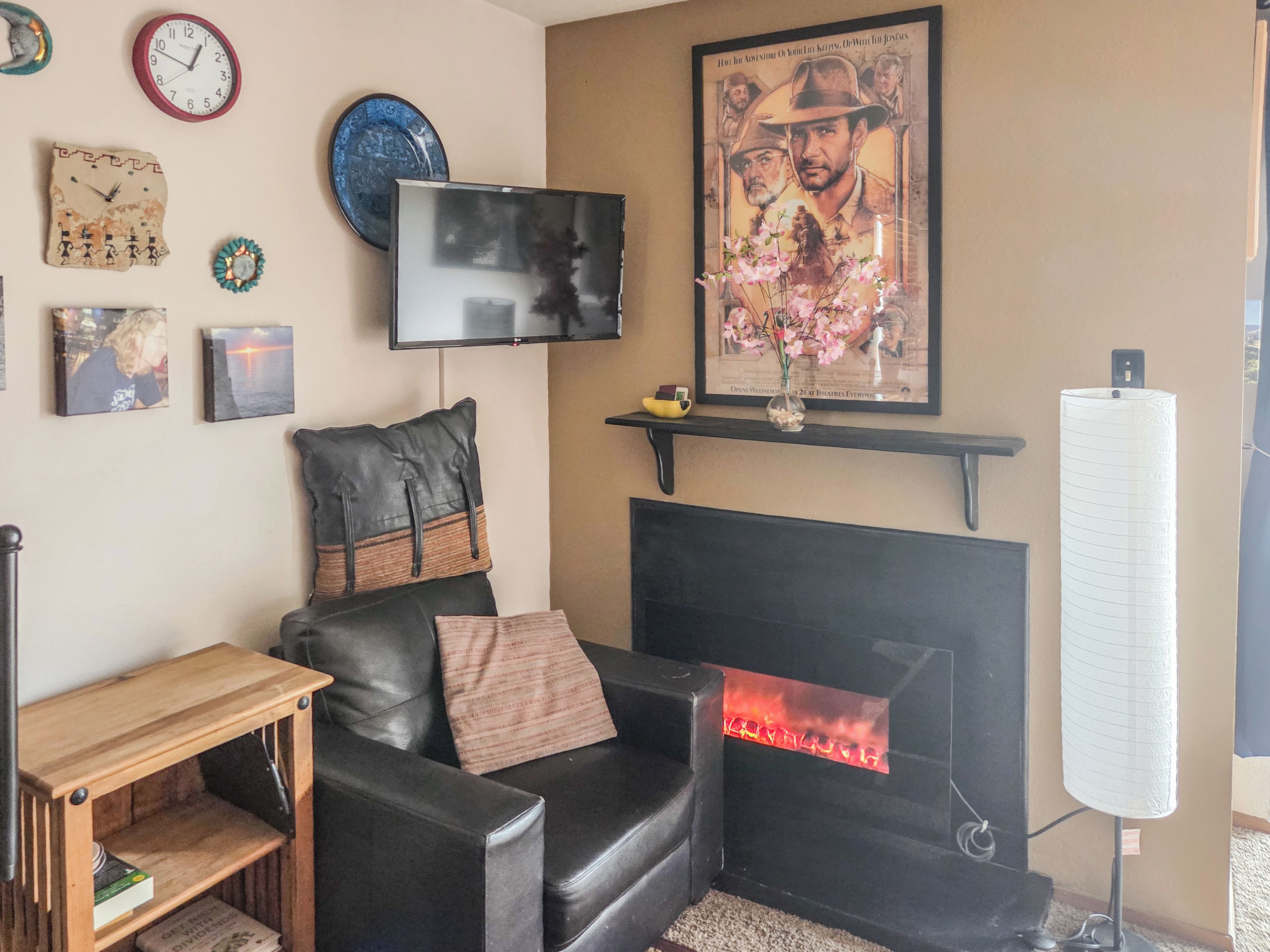 Ein Wohnzimmer mit einem schwarzen Ledersofa, einem an der Wand befestigten Flachbildfernseher, einem Kamin mit rotem Schein und einer Wanduhr.