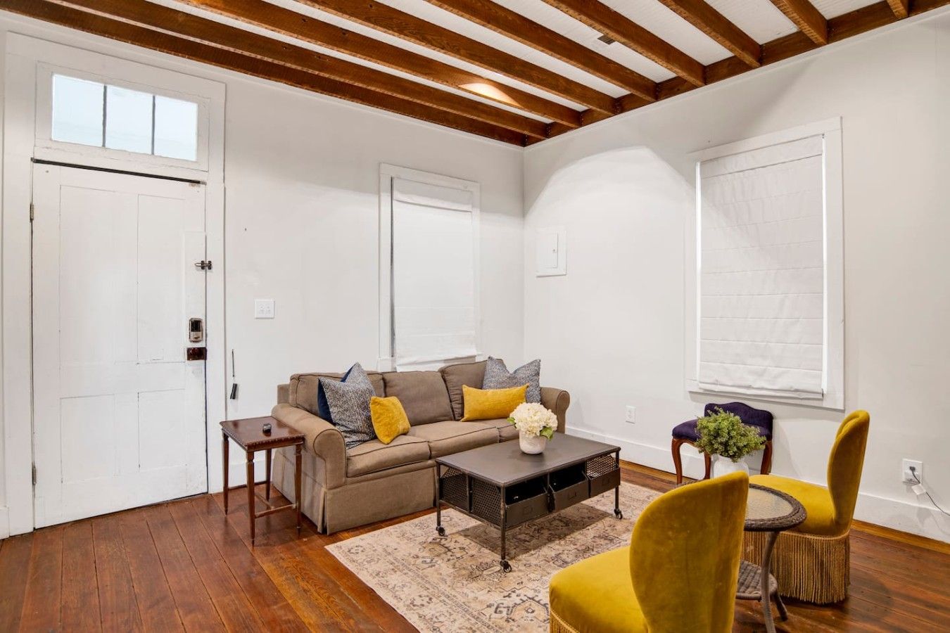 A living room with a wooden ceiling, a beige sofa with cushions, a coffee table, and a yellow armchair.