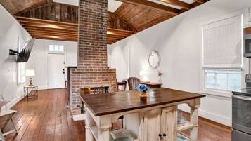 Una habitación amplia con una gran mesa de madera, una chimenea de ladrillo y una zona de cocina moderna.