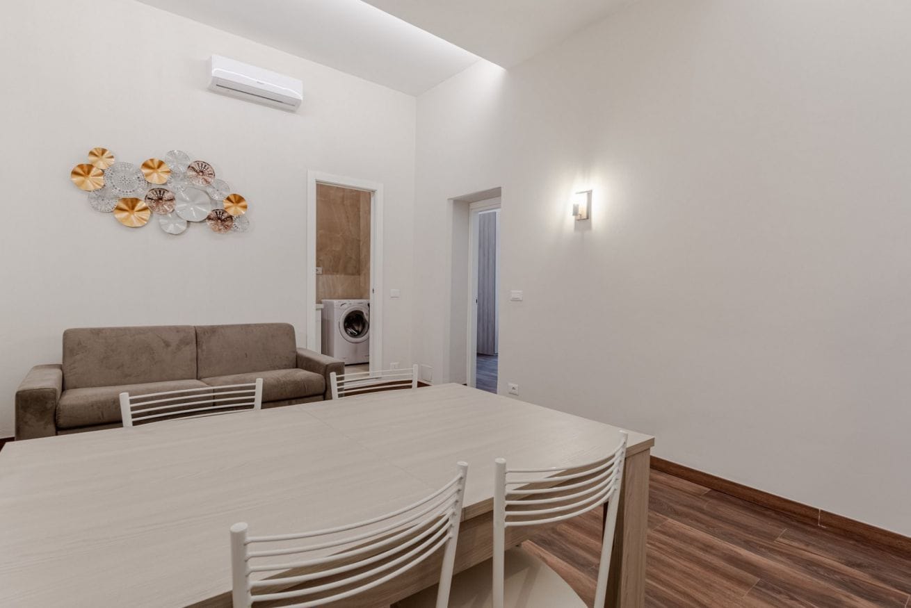 Una sala de estar moderna con un sofá, una mesa de comedor con sillas, una lavadora y un aire acondicionado instalado en la pared.
