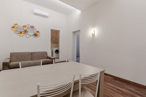 Uma sala de estar moderna com sofá, mesa de jantar com cadeiras, máquina de lavar roupa e ar condicionado fixado na parede.