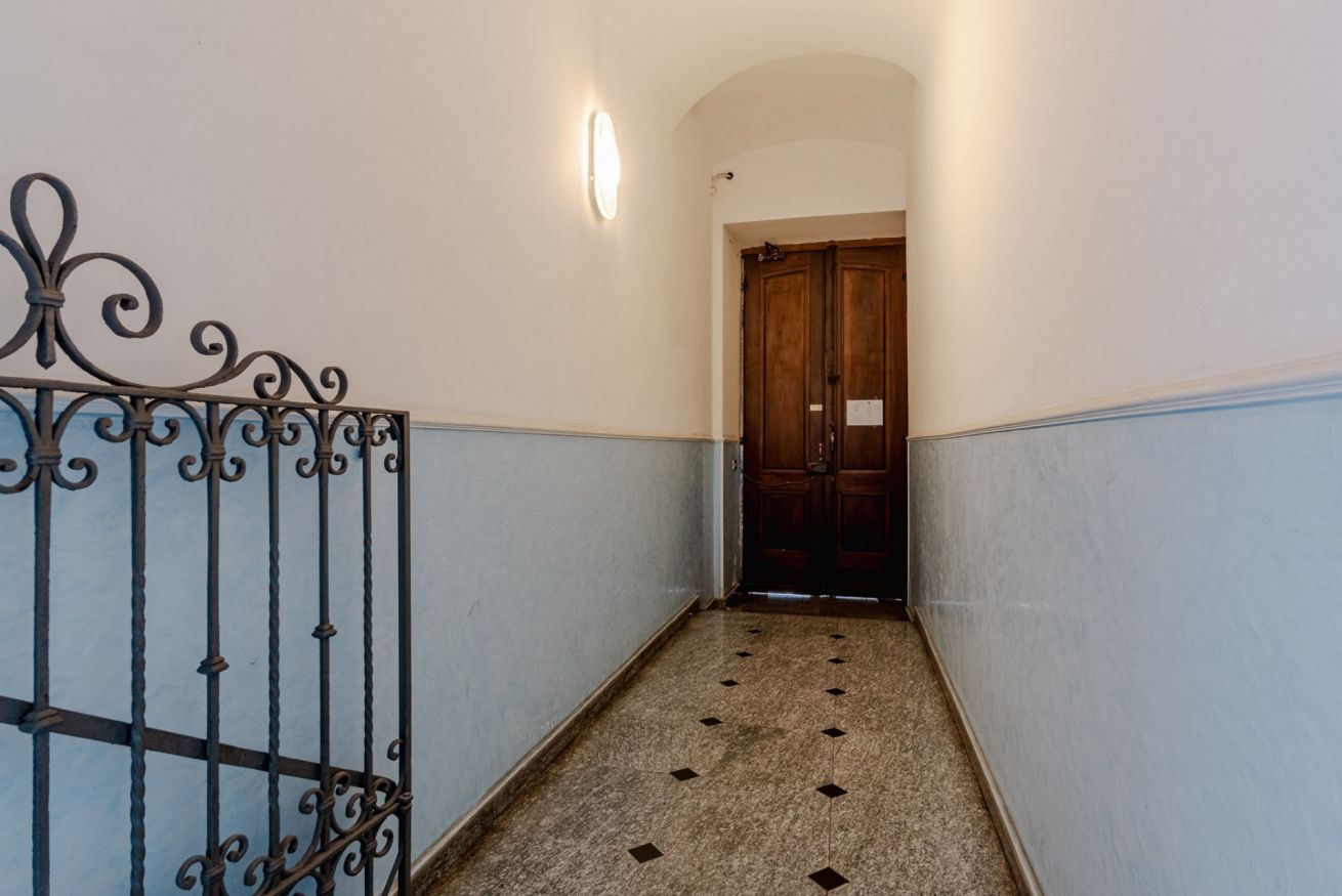Un pasillo con barandilla de metal, una puerta de madera al final e iluminación en la pared.