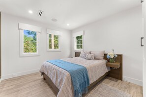 Ein Schlafzimmer mit einem Bett, einem Nachttisch, einem Fenster und einer Tür.