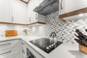A modern kitchen with white cabinets, a black induction cooktop, and a stainless steel kettle. - Immaculate new villa, steps to Kiawah's famous beaches (Kiawah Island)