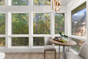 A room with large windows, a round table with a fruit platter, and a chair. - Immaculate new villa, steps to Kiawah's famous beaches (Kiawah Island)