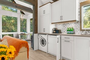A modern kitchen with white cabinets, a built-in washing machine, and a window overlooking greenery. - Immaculate new villa, steps to Kiawah's famous beaches (Kiawah Island)