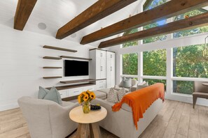 Ein modernes Wohnzimmer mit Flachbildfernseher, Einbauschränken, einer Couch und einem großen Fenster mit Blick auf Grünflächen.