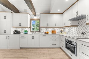 A modern kitchen with white cabinetry, a built-in oven, and a window with a view of greenery. - Immaculate new villa, steps to Kiawah's famous beaches (Kiawah Island)