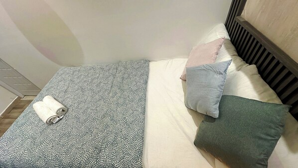 A small, neatly made bed with a patterned bedspread, a rolled-up towel, and three pillows in different colors. - Pathfinder Partition Room in Tecom (Dubai)