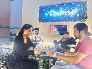A group of people seated at outdoor tables with a neon sign in the background. - Pathfinder Partition Room in Tecom (Dubai)