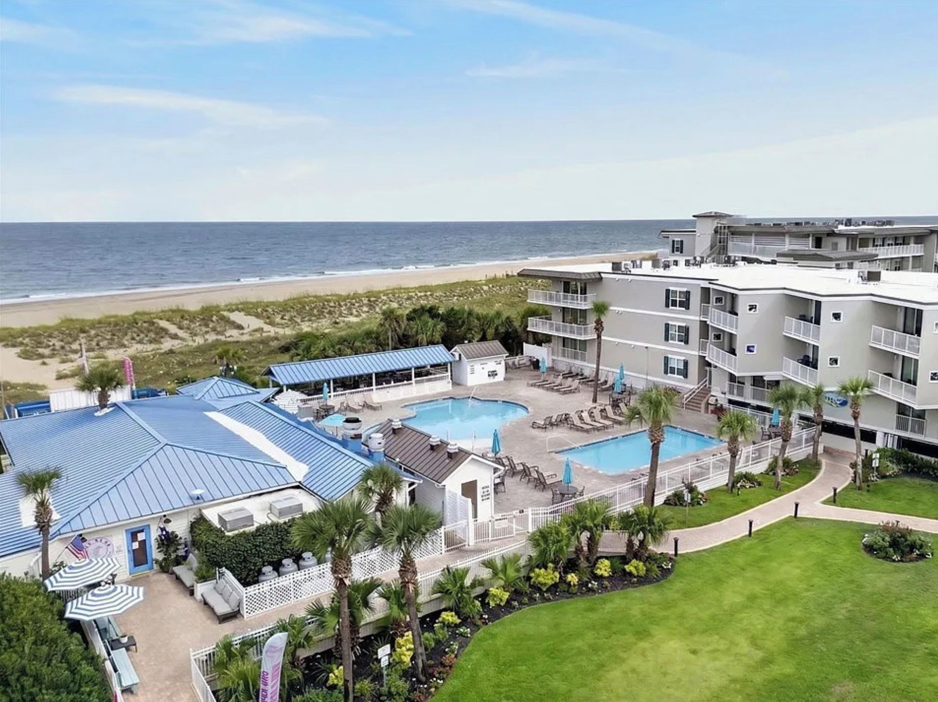 A hotel with multiple swimming pools, a beach view, and a well-maintained lawn.