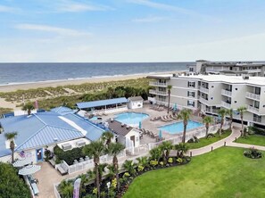 Ein Hotel mit mehreren Schwimmbecken, Blick auf den Strand und einer gepflegten Rasenfläche.