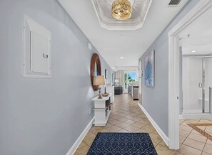 Un couloir d’hôtel avec une porte blanche, un miroir, une console et un tapis à motifs.