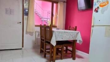 A dining area with a table set for two, a white refrigerator, and a television mounted on the wall.