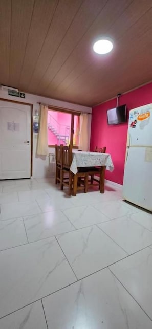Uma sala de jantar com mesa posta para dois, uma geladeira branca e uma televisão na parede.