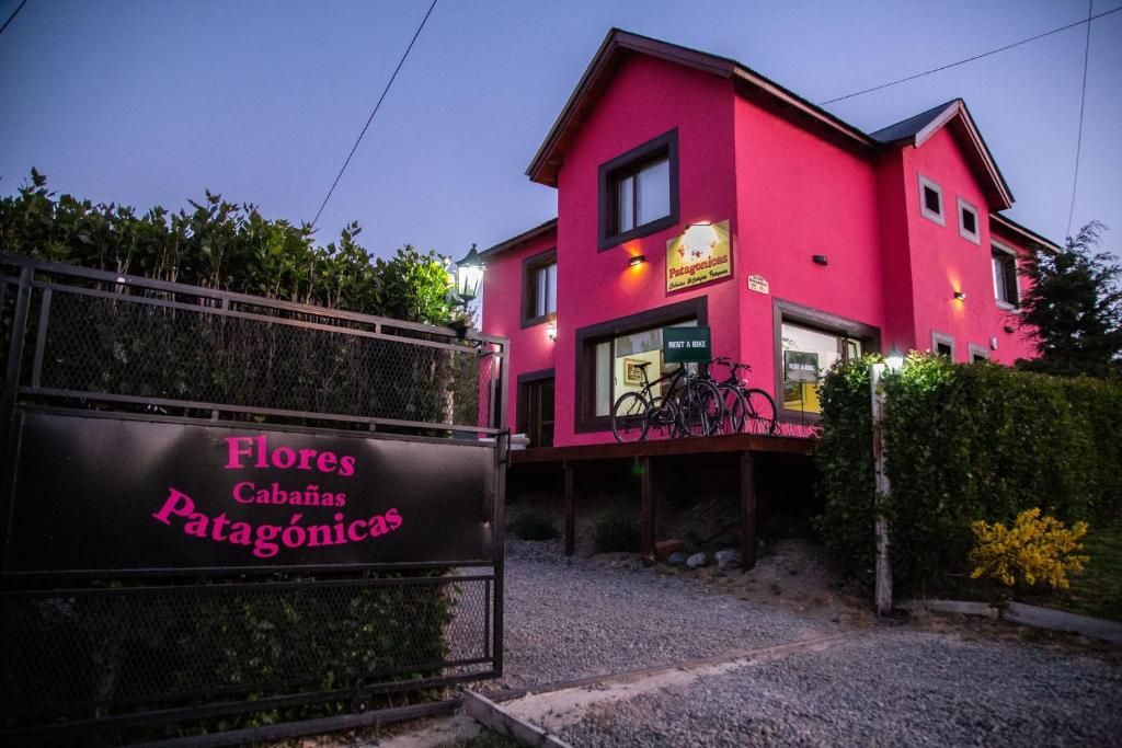 Un edificio rosa con un letrero que dice 'Flores Cabañas Patagonia' y una bicicleta estacionada afuera.