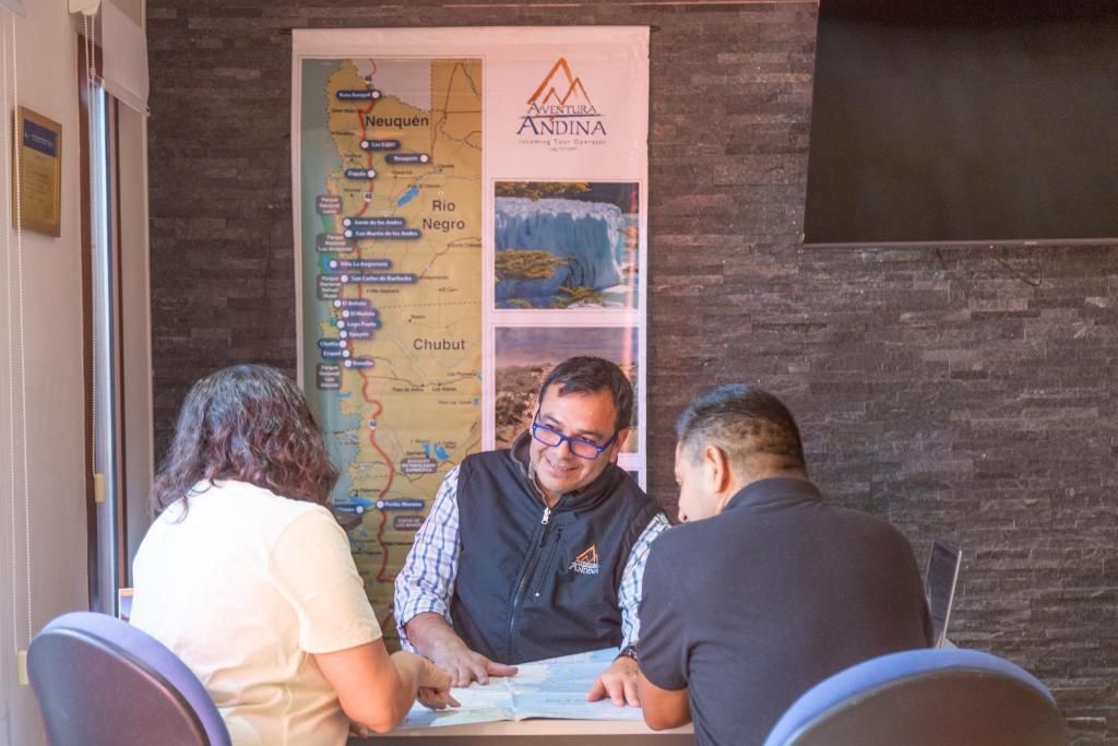 Un grupo de personas sentadas a una mesa con un mapa y un folleto frente a ellas.