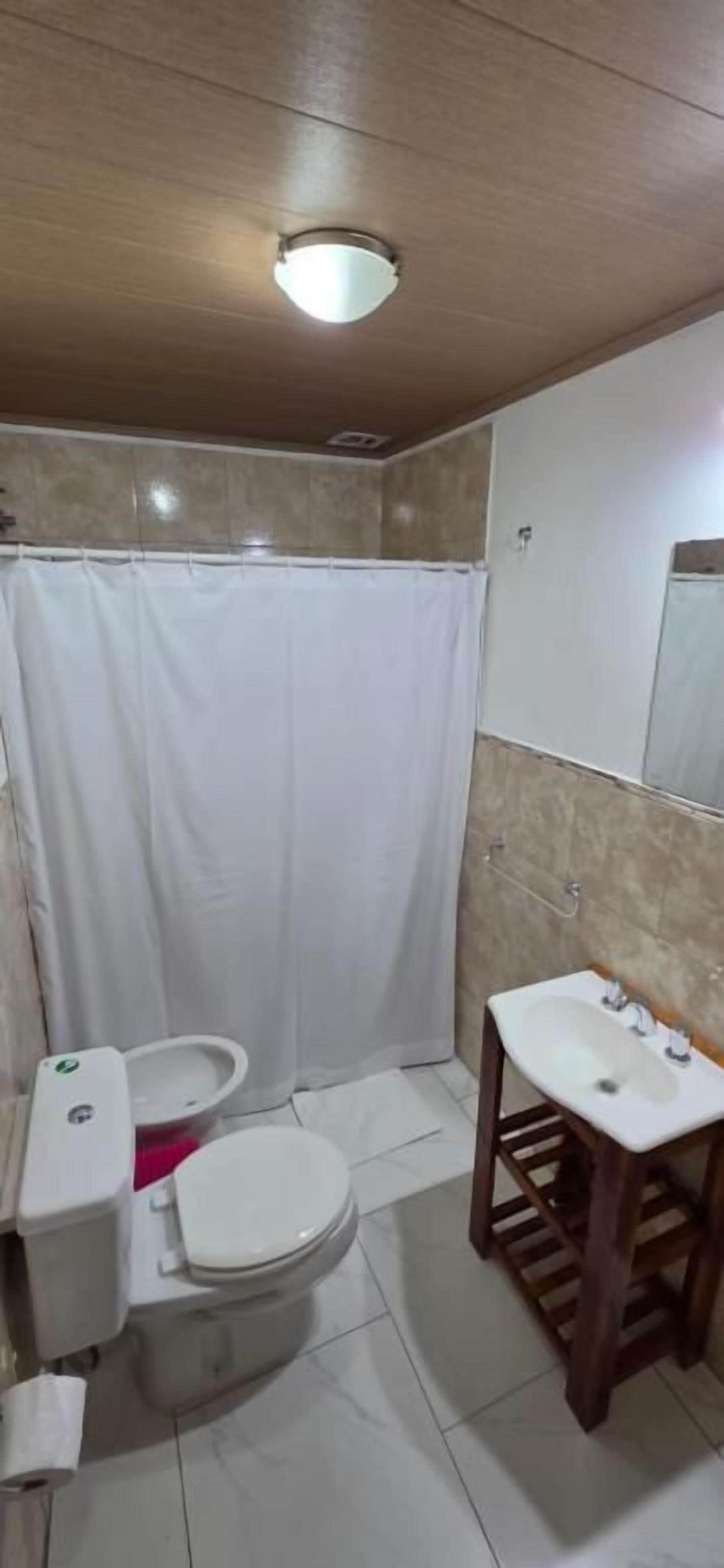 A bathroom with a toilet, bidet, sink, and shower curtain.
