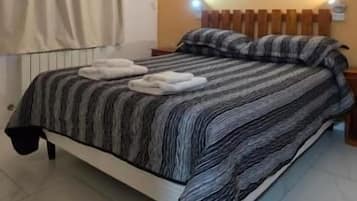 A bedroom with a bed, curtains, a wall-mounted light, and a framed picture.
