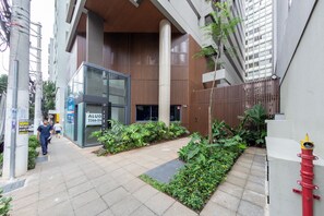 A modern building with a glass entrance, a fire hydrant, and a planter with tropical plants. - Plona by Bhomy (São Paulo)