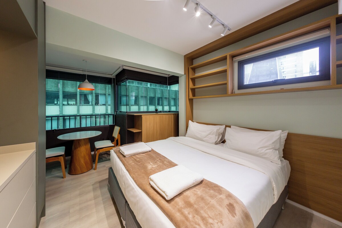 A hotel room with a bed, a desk, a chair, a window, and a view of the city.