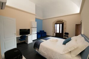 Una habitación de hotel con cama, escritorio, televisor y zona de estar con sillones.