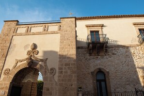 A stone building with a weather vane, a balcony with a wrought iron railing, and a door with a decorative arch. - Baglio dei Mori - Suite with kitchen and terrace in a 12th-century palace (Donnalucata)