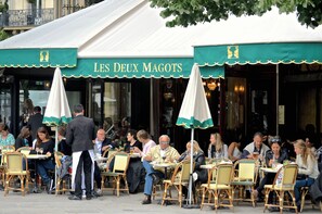 An outdoor cafe with tables and chairs, a sign reading 'LES DEUX MAGOTS', and a person standing in front of the cafe. - Elegant Saint-Germain Retreat with Parisian Charm in the Heart of Paris (Paris)