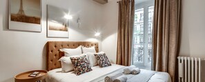 A hotel room with a bed, a bedside table, a wall-mounted light, a window with curtains, and a radiator. - Elegant Saint-Germain Retreat with Parisian Charm in the Heart of Paris (Paris)