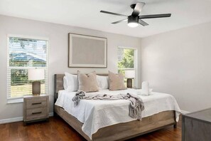 A bedroom with a bed, bedside tables, a ceiling fan, and windows.