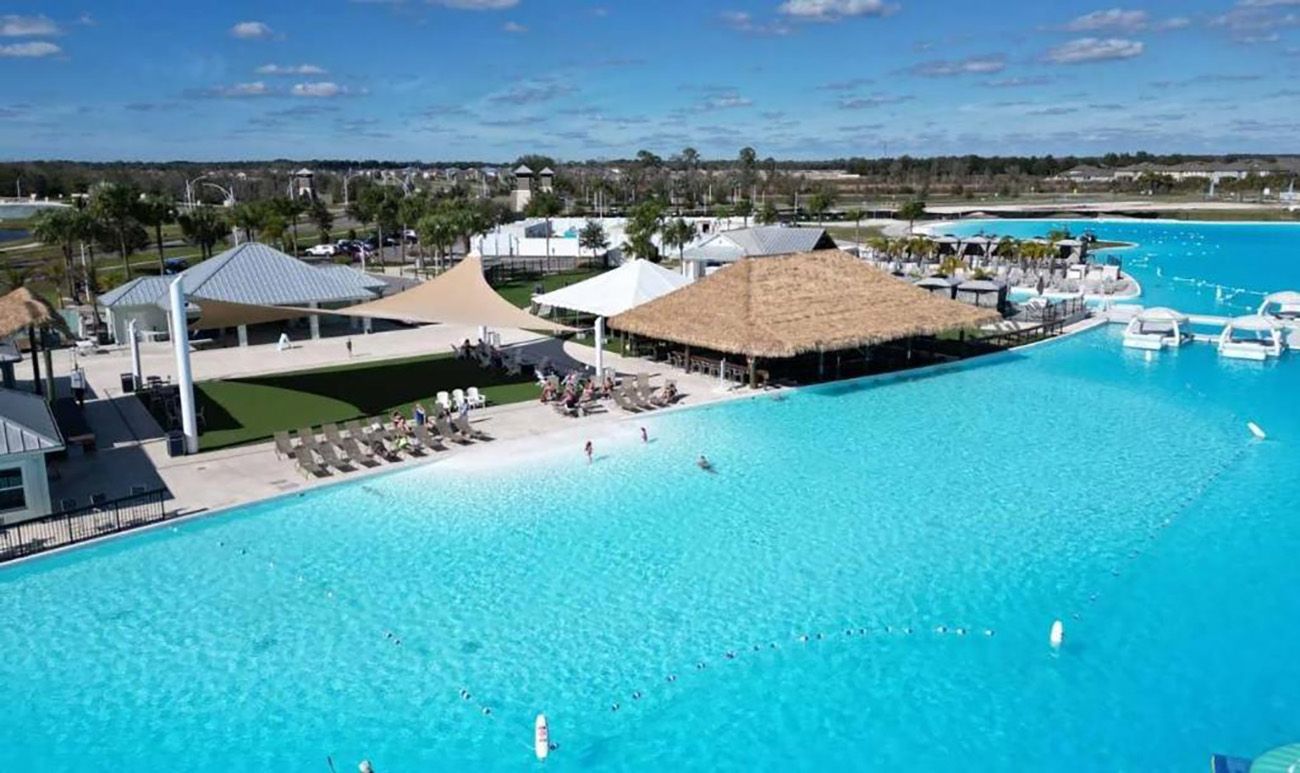 A large swimming pool with a thatched-roof structure, lounge chairs, and boats.