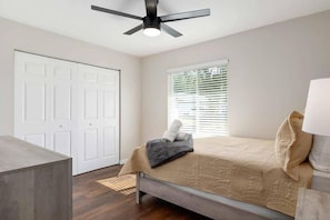 A bedroom with a bed, a ceiling fan, a window with blinds, and a door.
