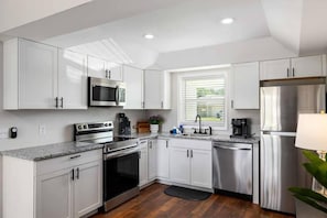 A modern kitchen with white cabinets, stainless steel appliances, and a window providing natural light.