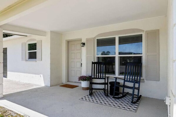 A porch with two rocking chairs, a potted plant, and a checkered rug.