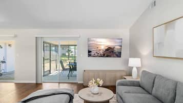 A modern living room with a grey sofa, a coffee table with flowers, and a painting of a sunset.