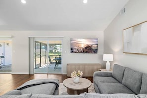 A modern living room with a grey sofa, a coffee table with flowers, and a painting of a sunset.