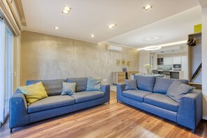 A modern living room with two sofas, wooden flooring, recessed ceiling lights, and a kitchen in the background. - Luxury 3-bed With Private Terrace in St Julian s (St. Julian's)