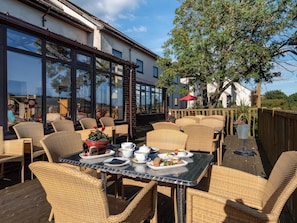 An outdoor dining area with wicker furniture and a table set for a meal. - Moorhen (Newton Abbot)