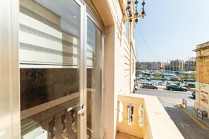 Blick von einem Balkon mit einer Glastür, die zu einem Zimmer führt, mit Blick auf einen Yachthafen, mit Booten und Gebäuden im Hintergrund.
