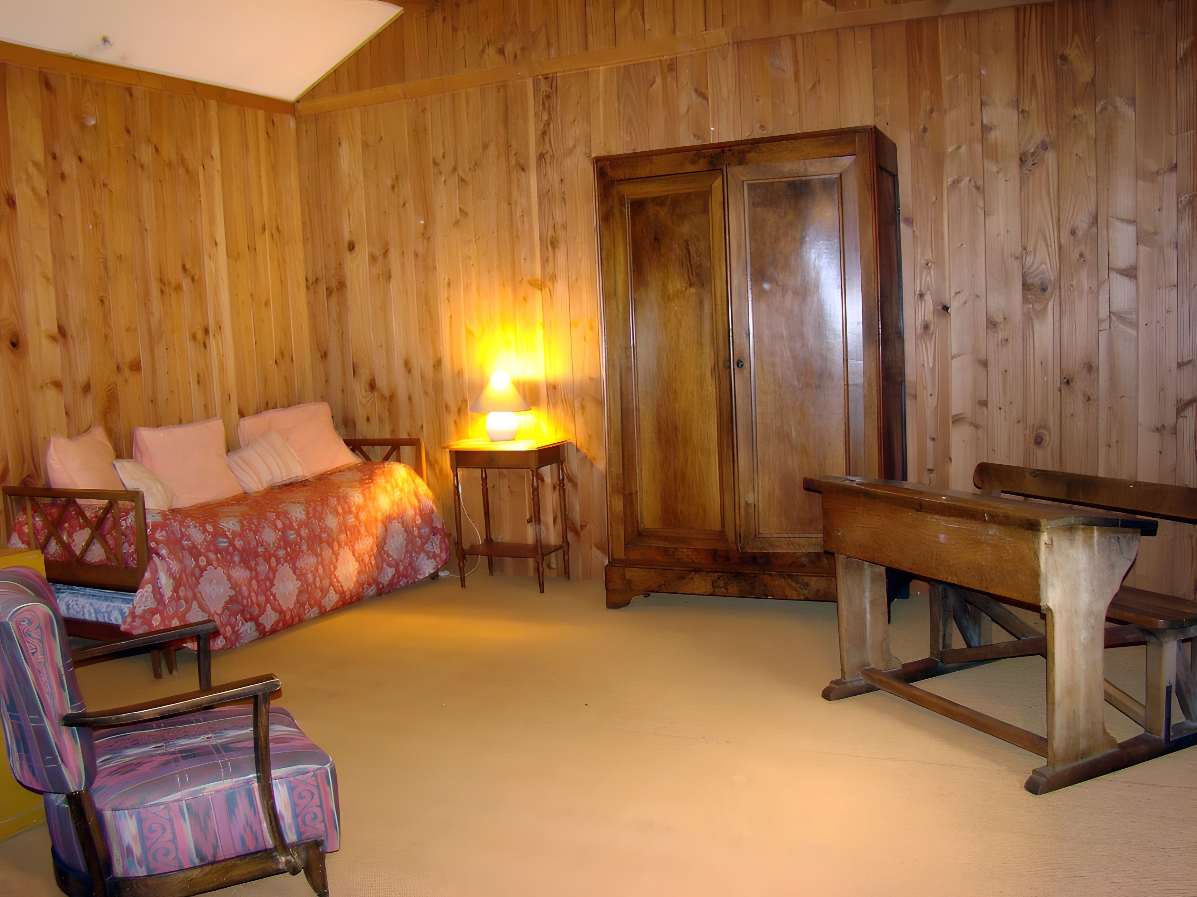 A room with a bed, a chair, a table, and a wardrobe.