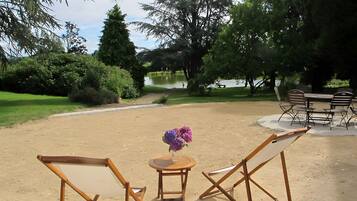 Un espace extérieur aménagé avec une table et des chaises, entouré d’arbres et bordé par un plan d’eau.