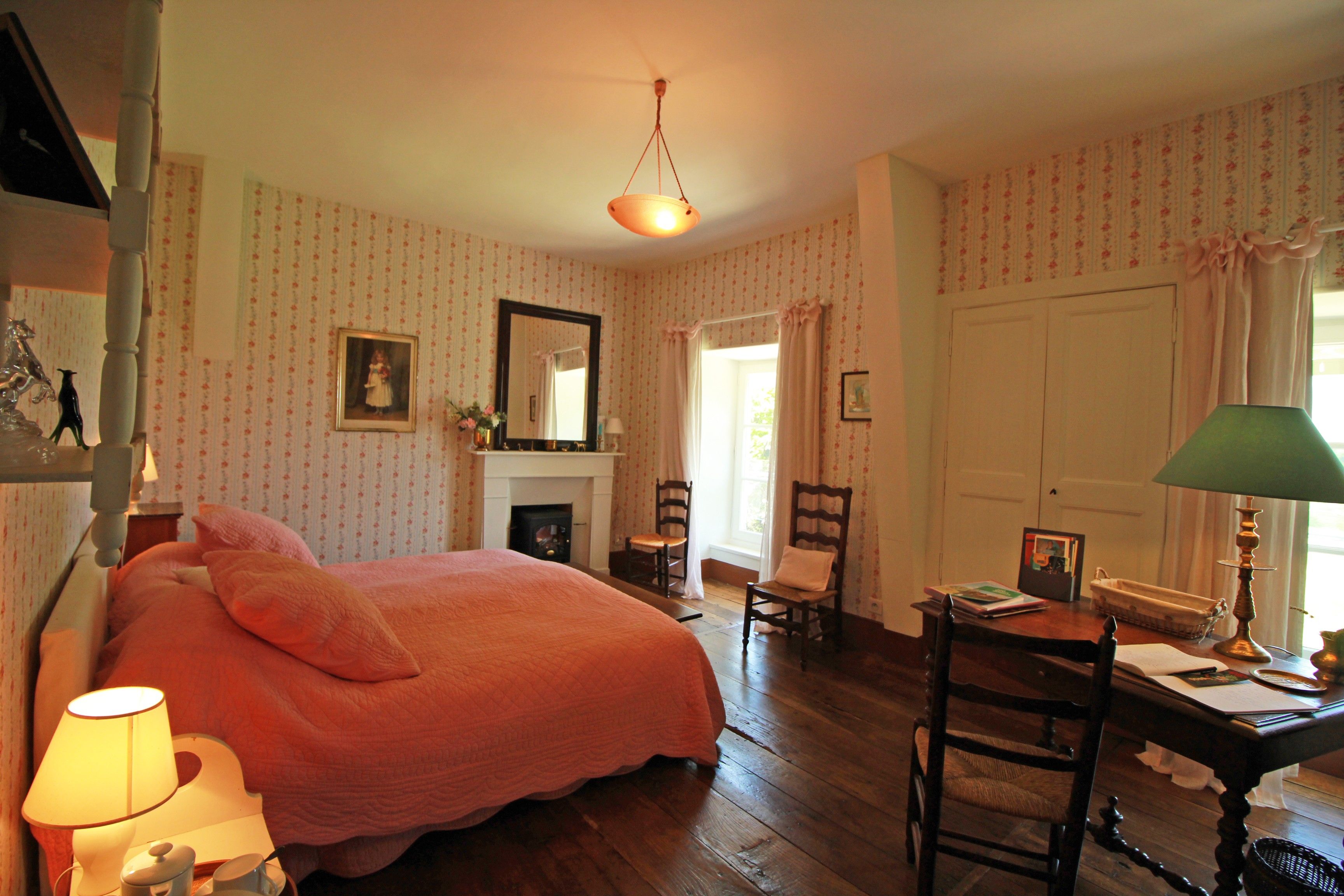 Een slaapkamer met een groot bed, een open haard, een bureau met een lamp en een stoel.