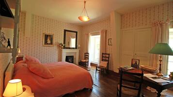 Een slaapkamer met een groot bed, een open haard, een bureau met een lamp en een stoel.