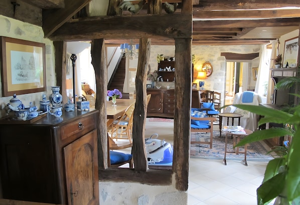 A rustic interior with exposed wooden beams, a dining area with blue chairs, and a staircase leading to another level.