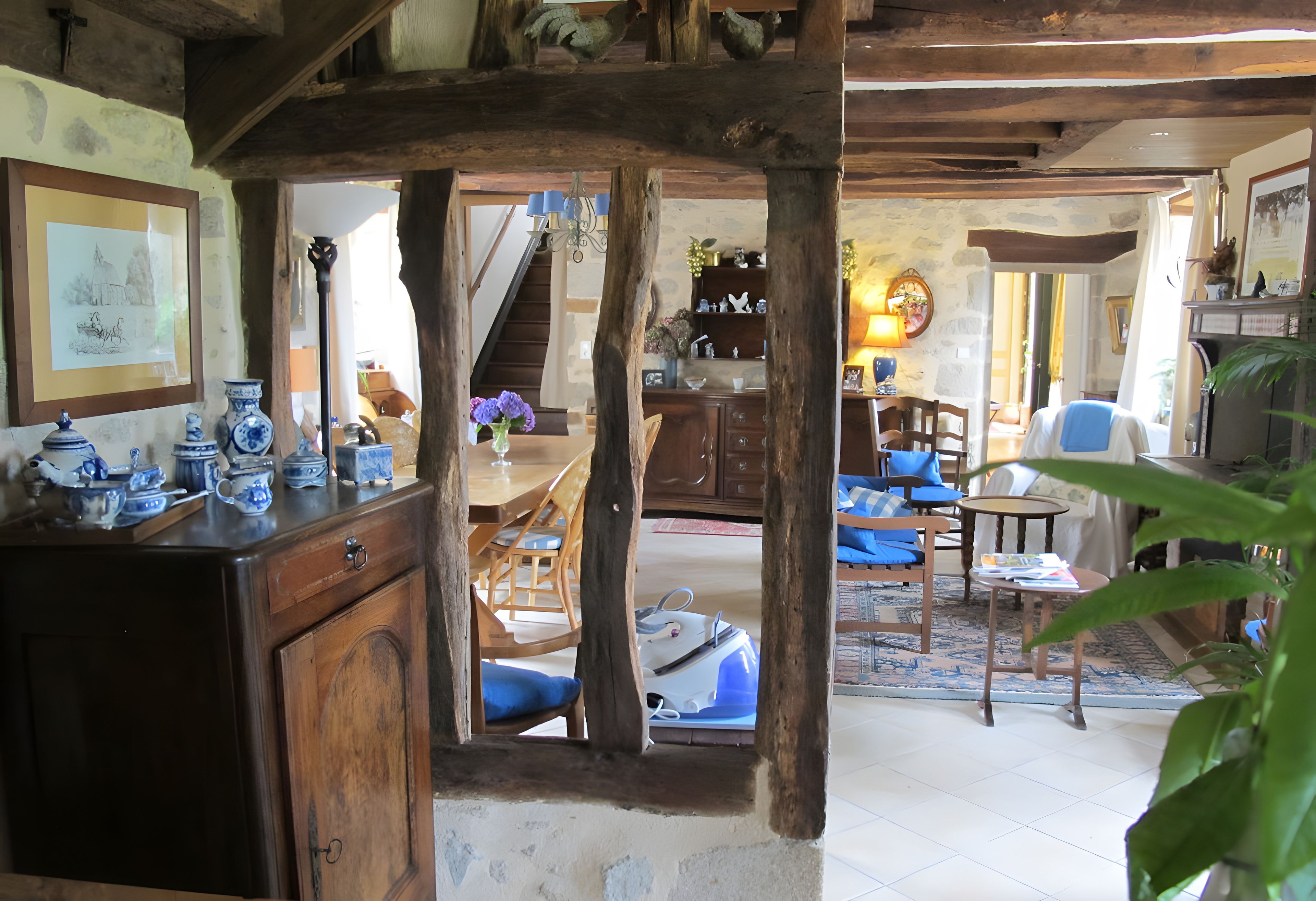 Un intérieur rustique avec des poutres apparentes, un coin repas avec des chaises bleues et un escalier menant à un autre niveau.