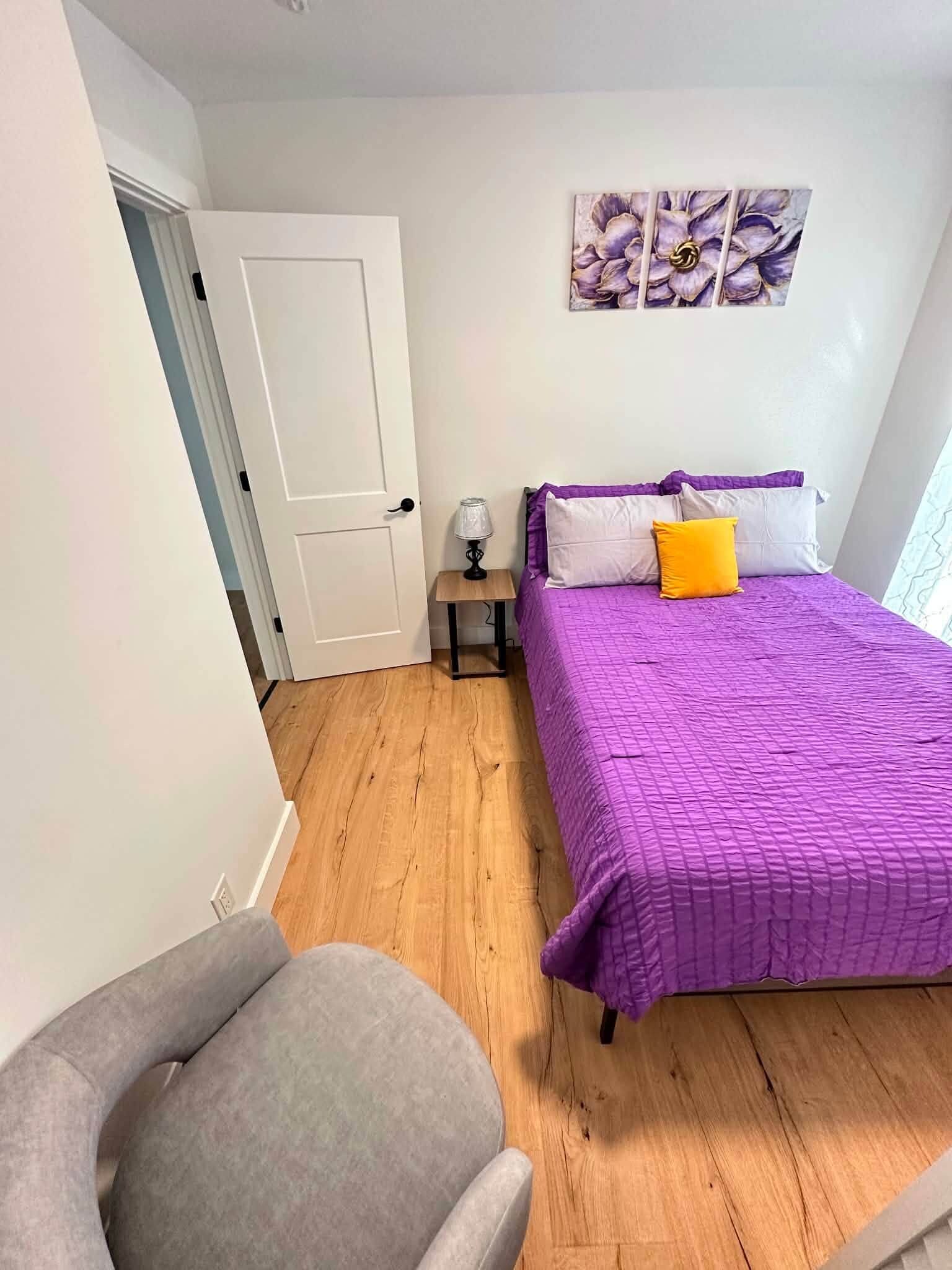Ein Schlafzimmer mit einem Bett, einem Sessel, einem Nachttisch und einer Tür.