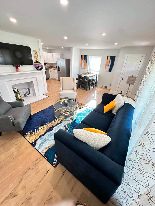 A modern living room with a dark blue sofa, a glass coffee table, and a patterned rug.