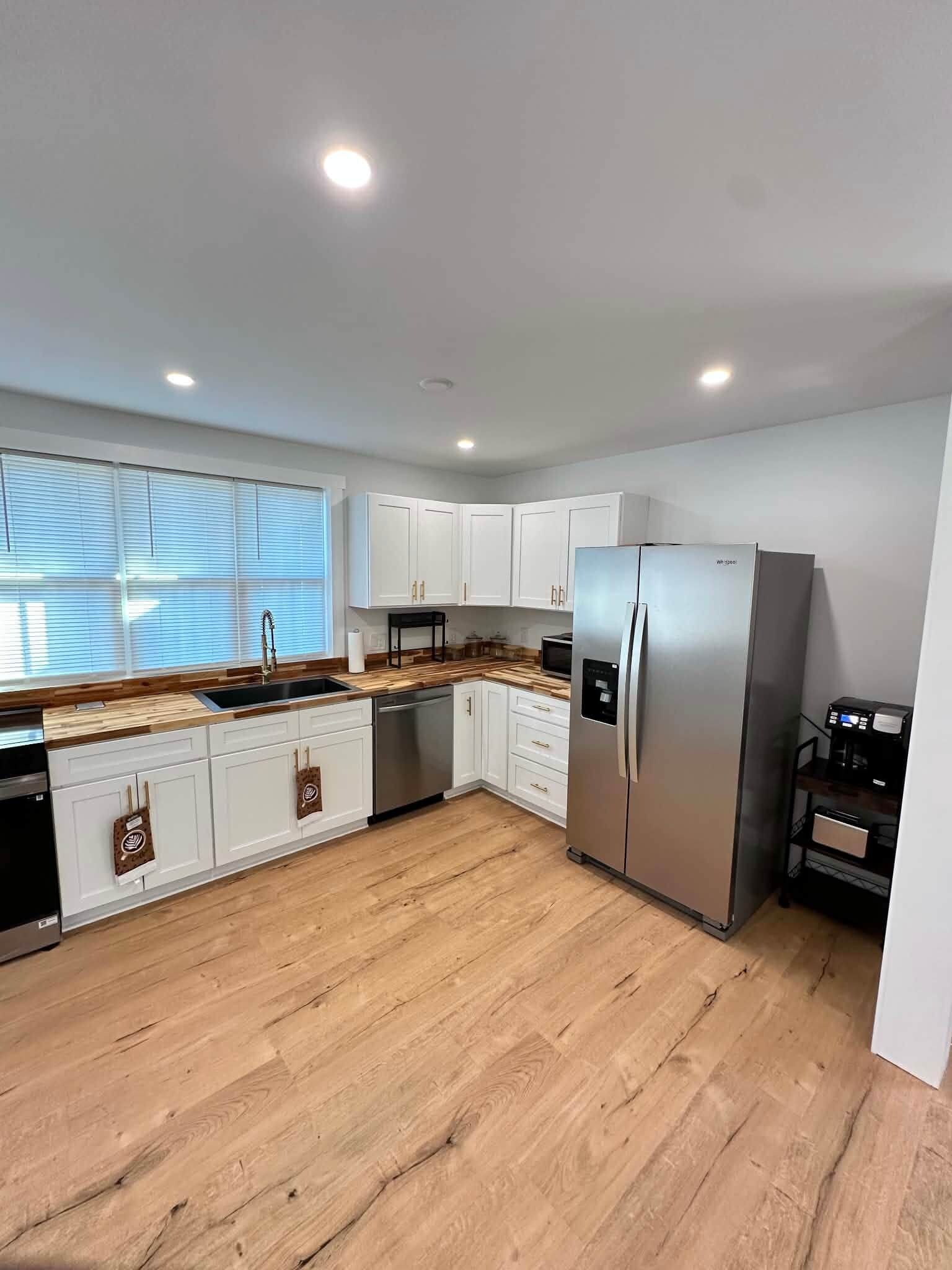 A modern kitchen with white cabinets, a stainless steel refrigerator, and a wooden countertop.