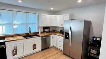 A modern kitchen with white cabinets, a stainless steel refrigerator, and a wooden countertop.