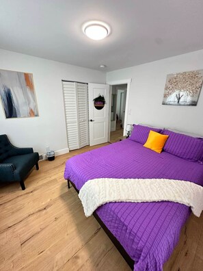 A bedroom with a bed, a chair, a door, and a painting on the wall. - Eden House: Your cozy retreat in High Point (High Point)